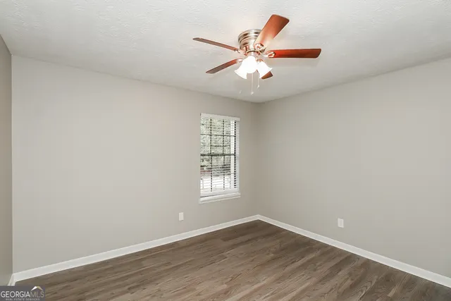 an empty room with wooden floor fan and windows