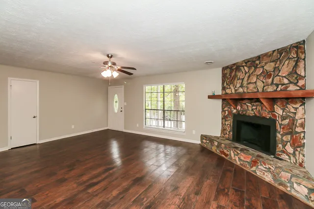 a view of an empty room with wooden floor fireplace and a window