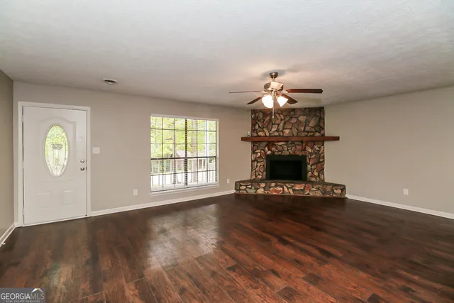 a view of an empty room with wooden floor fireplace and a window