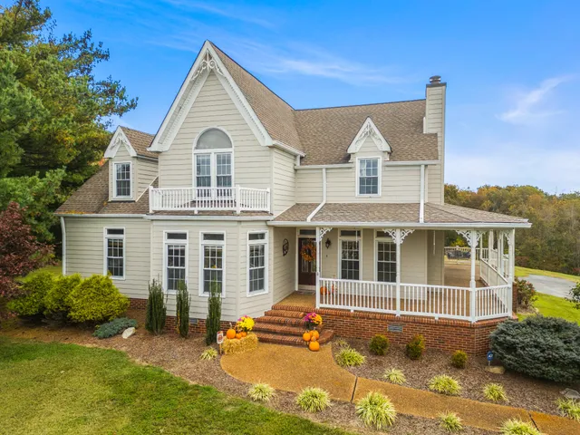 a view of a white house with a large windows and a yard with plants and large tree