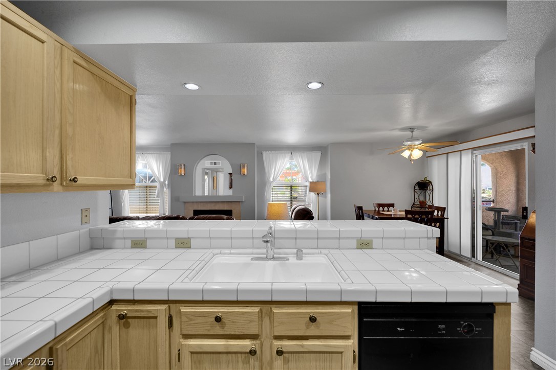 7570 West Flamingo Road, Unit 115 Las Vegas, NV 89147 - Photo 11 of 34 A classic kitchen with tiled countertops overlooks a living area with a fireplace and ample natural light.
