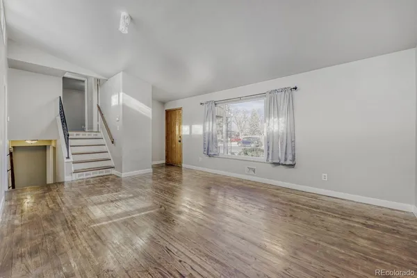 a view of an empty room with wooden floor and stairs