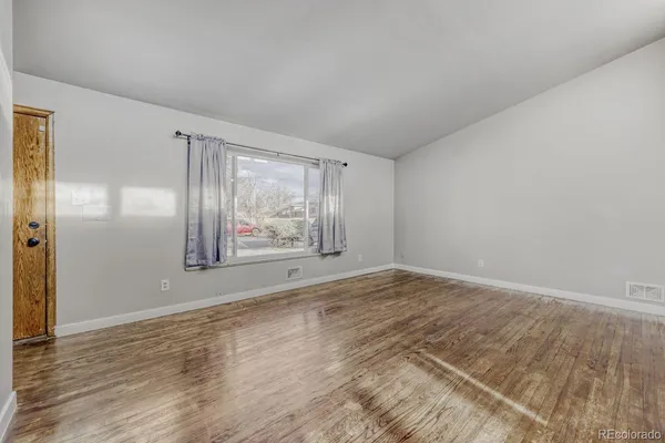 a view of an empty room with wooden floor and a window