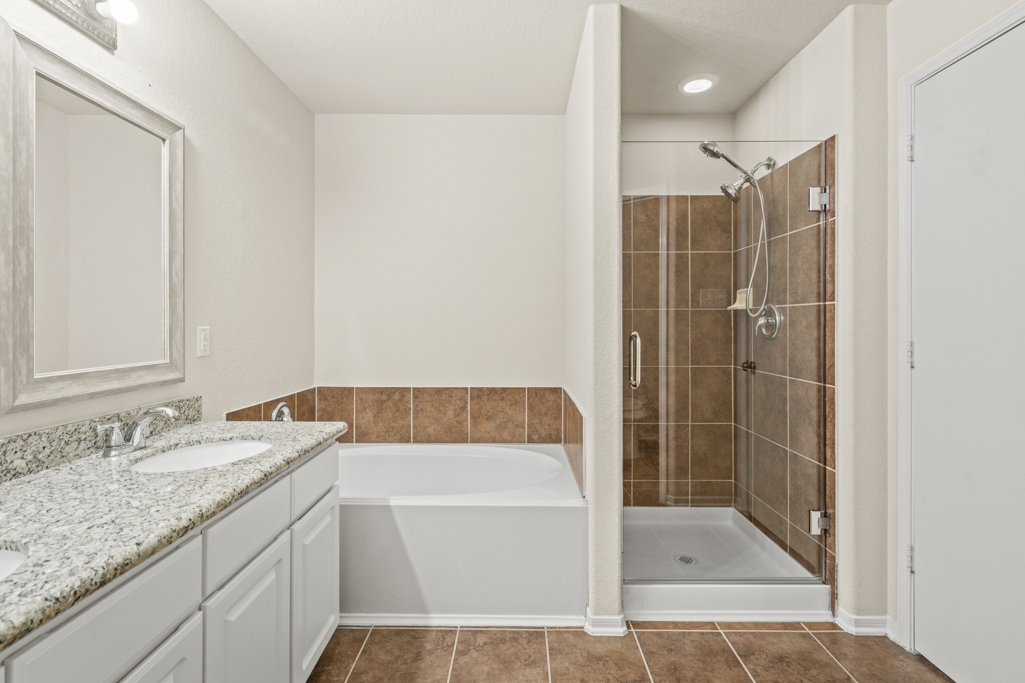 3118 Winchester Rnch Trail Katy, TX 77493 - Photo 15 of 22 The primary bathroom is a true spa-inspired retreat, featuring a deep soaking tub with elegant tile surround, a glass-enclosed walk-in shower with rich brown tile walls, a granite vanity with white cabinetry, framed mirror, and recessed lighting — everything you need to unwind and recharge at the end of the day.