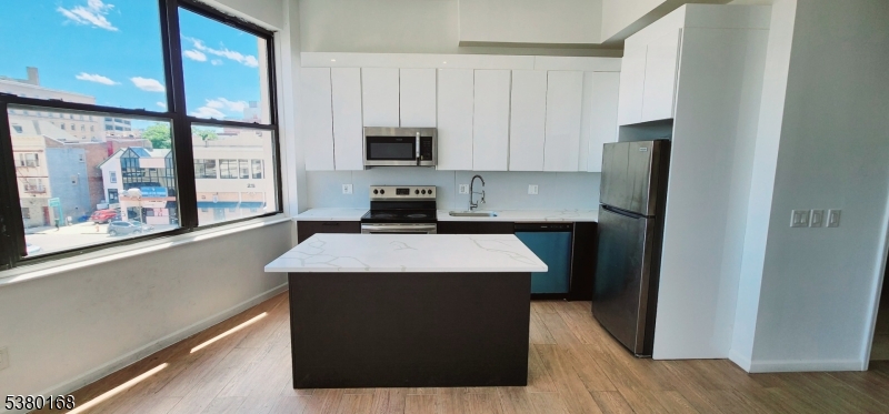 30 Howe Avenue, Unit 304 Passaic, NJ 07055 - Photo 9 of 12 a kitchen with stainless steel appliances kitchen island granite countertop a refrigerator a stove and a sink with wooden floor