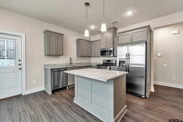 a kitchen with stainless steel appliances granite countertop a refrigerator a sink dishwasher a stove and white cabinets with wooden floor