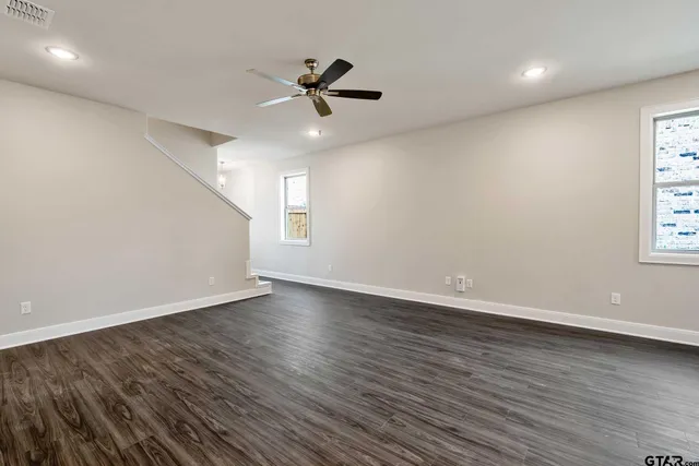 an empty room with wooden floor fan and windows
