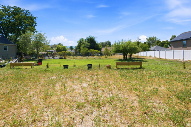 300 East S, Unit 2 Logan, UT 84321 - Photo 14 of 38 Expansive lot with partial grass coverage, featuring a mature tree, a white vinyl privacy fence, and distant mountain scenery