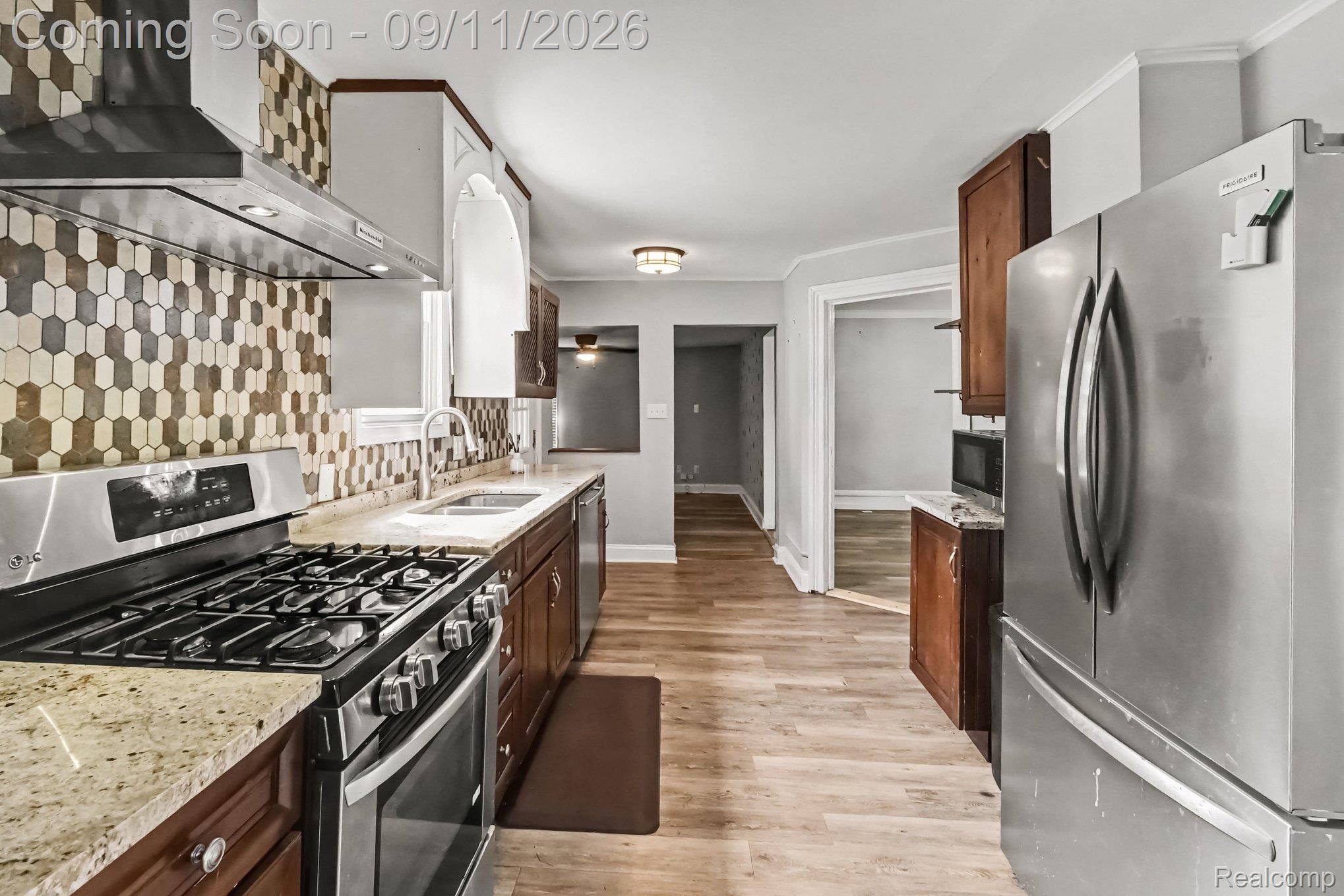 409 Fleming Street Howell, MI 48843 - Photo 5 of 25 Stainless steel range with coordinating hood, hexagonal tile backsplash, light-toned wood-finish flooring, and stainless steel refrigerator