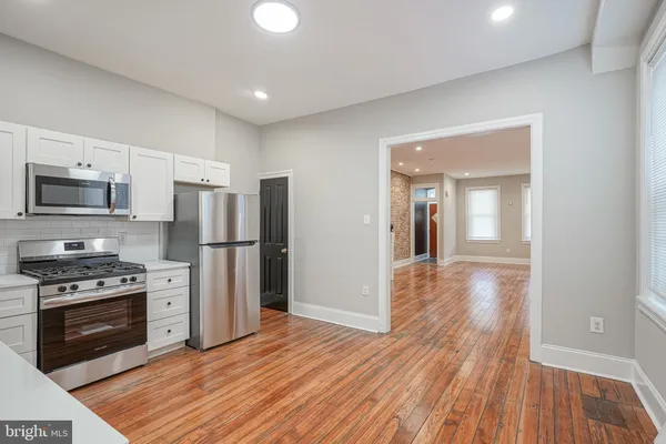 a kitchen with stainless steel appliances a stove top oven a refrigerator cabinets and wooden floor
