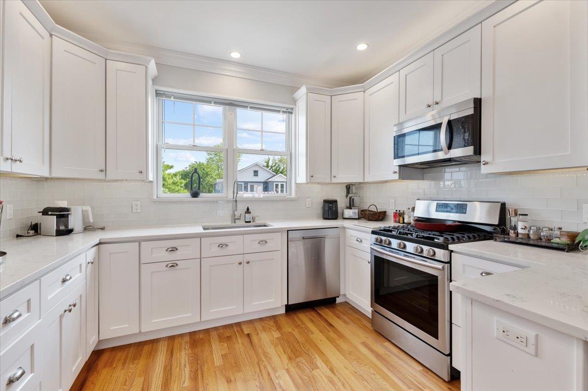 545 East Fulton Street Long Beach, NY 11561 - Photo 3 of 41 Kitchen with stainless steel appliances, white cabinets, crown molding, backsplash, and light wood-type flooring