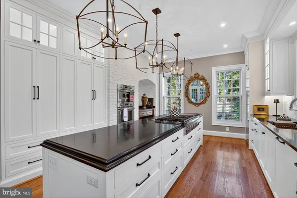 a kitchen with stainless steel appliances granite countertop a sink a stove top oven a chimney cabinets and wooden floor