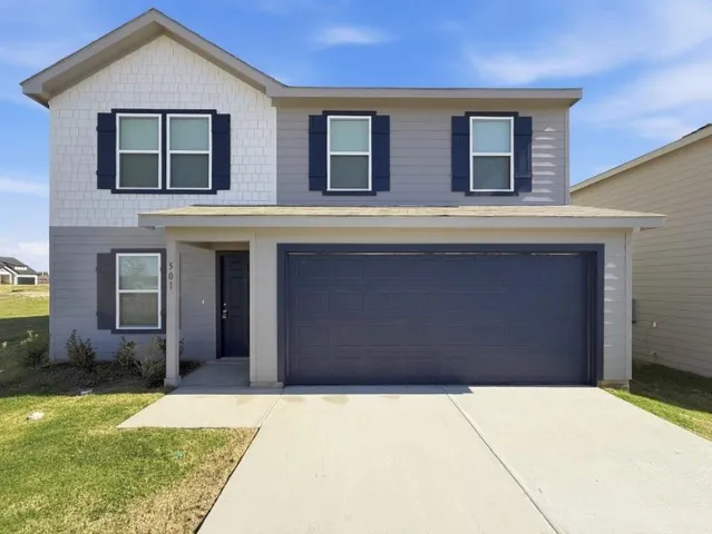 a view of a brick house with a yard plants and large tree