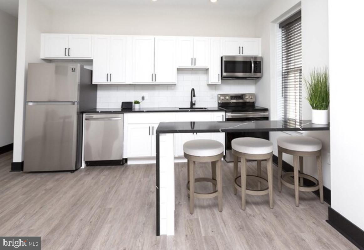 938 North Calvert Street, Unit 1B Baltimore, MD 21202 - Photo 2 of 11 a kitchen with stainless steel appliances granite countertop a stove a sink a microwave a refrigerator and white cabinets with wooden floor