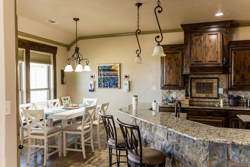 123 Cactus Drive Decatur, TX 76234 - Photo 8 of 30 Stone-front breakfast bar with granite countertop, dark wood-finish cabinetry, tile backsplash with decorative inset, and recessed lighting