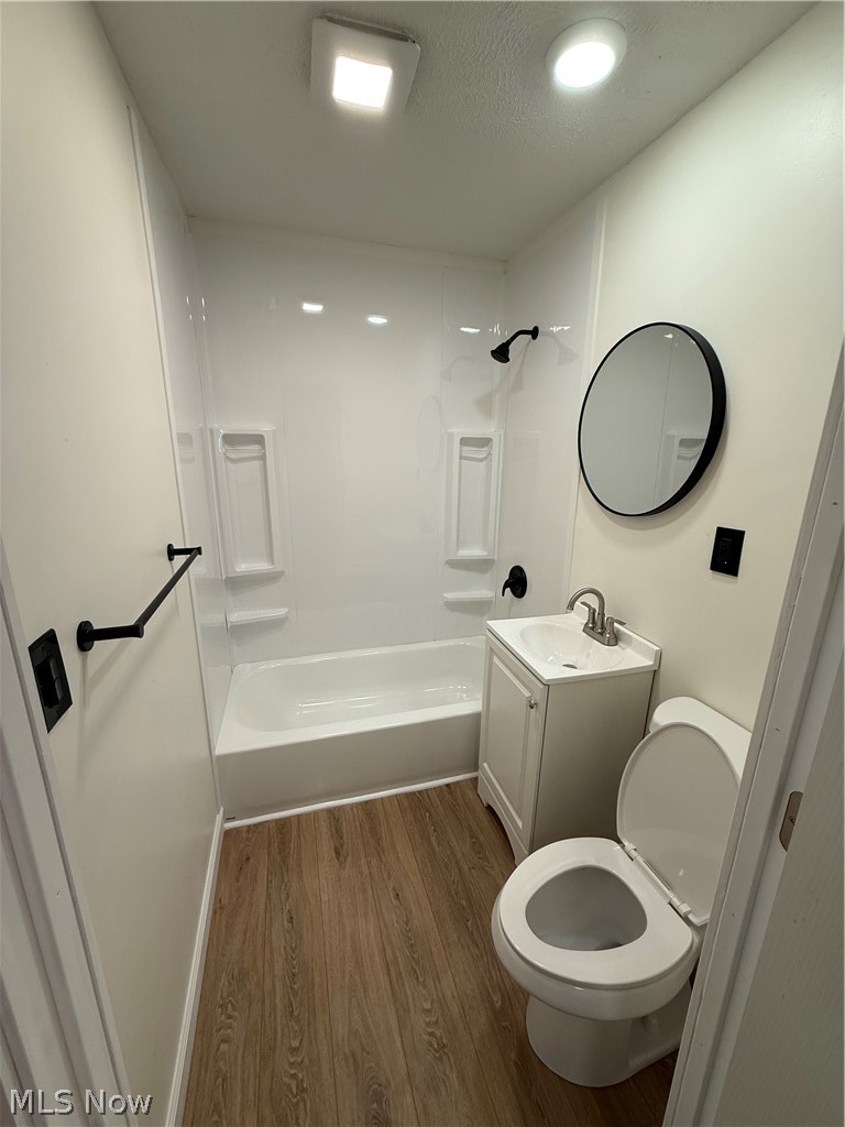4841 Marigold Road Mentor, OH 44060 - Photo 10 of 12 Compact bathroom featuring a white tub/shower combination with integrated shelving, a white single-sink vanity, wood-finish flooring, and a circular mirror with a black frame