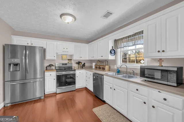 a kitchen with granite countertop a refrigerator oven a sink dishwasher and white cabinets with wooden floor