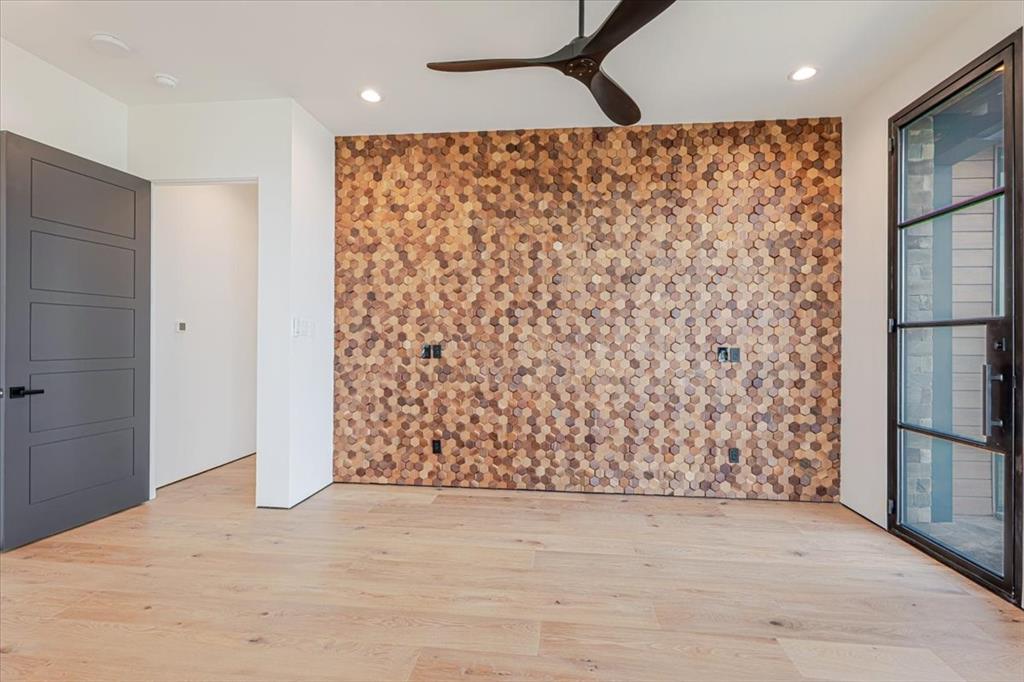 1014 Chaparrel Lane Graford, TX 76449 - Photo 12 of 40 Primary Owner’s Suite - Privately tucked on the opposite side of the great room from the secondary bedrooms, the Primary Owner’s Suite offers both seclusion and style. A stunning wood-accented feature wall adds texture and warmth to the bedroom, creating a striking contrast to the otherwise minimalist palette. Wide-plank, white oak floors flow seamlessly beneath your feet, continuing the home’s warm, sophisticated palette. Clean-lined and trimless, the room maintains an uncluttered aesthetic that frames the outdoors as the main event.