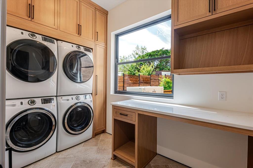 1014 Chaparrel Lane Graford, TX 76449 - Photo 17 of 40 The Hidden Hero of the Home - the Laundry Room! Function meets style in this beautifully appointed laundry room. With dual washers and dryers stacked neatly into custom cabinetry, laundry day becomes an efficient, streamlined affair. Generous upper cabinets offer abundant storage for supplies, while the quartz-topped folding counter provides a clean, spacious surface for sorting and organizing. The large picture window brings in natural light and frames a glimpse of the whole-house backup generator, offering peace of mind no matter the season. Wood tones echo the cabinetry throughout the home, tying this utility space into the home’s cohesive design.
