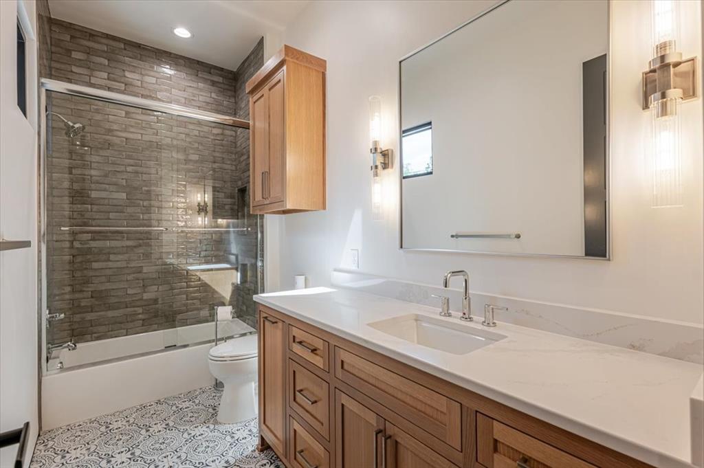 1014 Chaparrel Lane Graford, TX 76449 - Photo 20 of 40 Conveniently situated between the laundry room and staircase, this full bath serves the adjacent guest room and nearby office or flex space. It features a sleek, contemporary tub and shower surround with designer tile, generous vanity storage, and modern fixtures. A thoughtful layout makes this bathroom functional for both daily use and visiting guests.