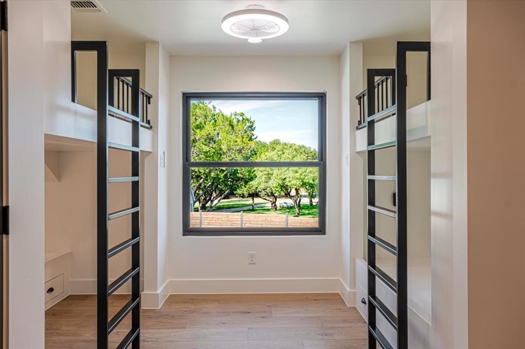 1014 Chaparrel Lane Graford, TX 76449 - Photo 28 of 40 Built-in Bunks with View - This inviting bunk space features four built-in bunks with modern black railings and ladders, each equipped with its own reading light and device charging station. A large window frames a serene, leafy view—making this the perfect hideaway for kids, guests, or grandkids.