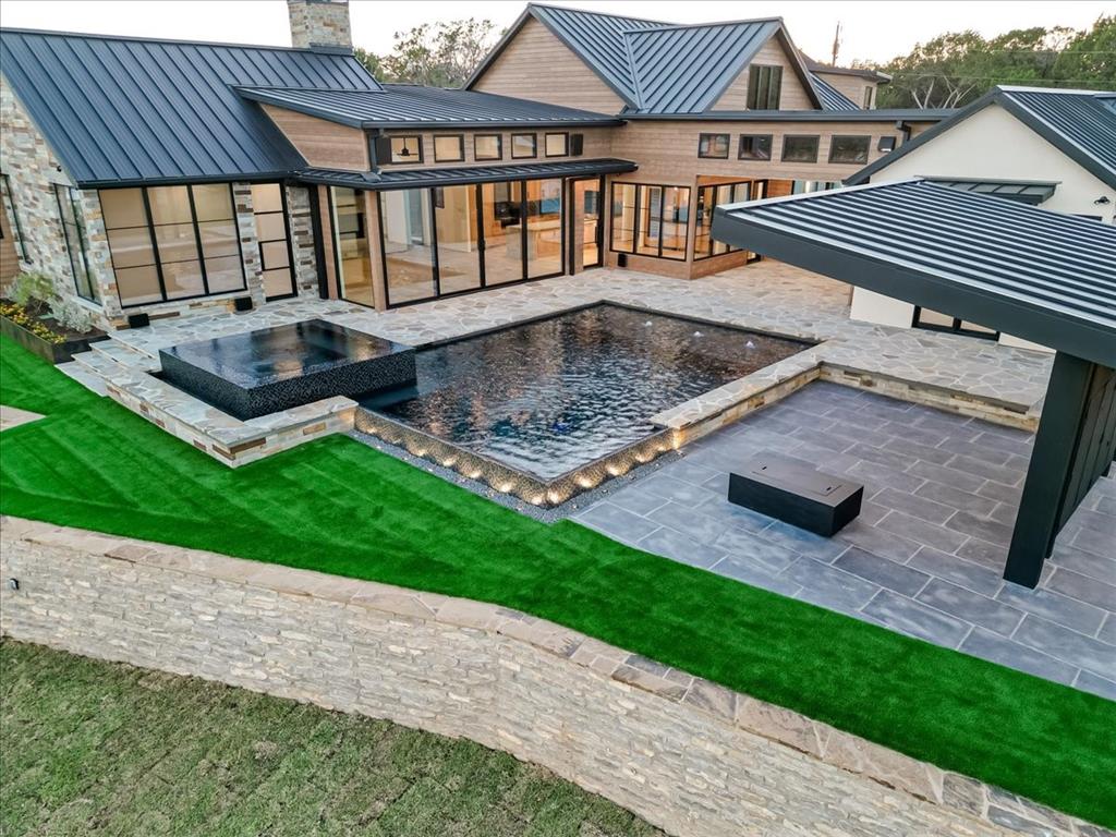 1014 Chaparrel Lane Graford, TX 76449 - Photo 31 of 40 Resort-Style Backyard with Premium Turf and Outdoor Living Spaces - From this elevated view, the home’s thoughtfully designed backyard unfolds—featuring a sleek pool and spa, flower beds edged in weathered steel, and soft evening lighting. The covered entertainment area with an 85” outdoor TV and modern fire pit invites year-round gatherings. Premium synthetic turf adds visual softness and practicality, staying cool underfoot and offering a natural look with easy upkeep—perfect for lounging, play, or pets.