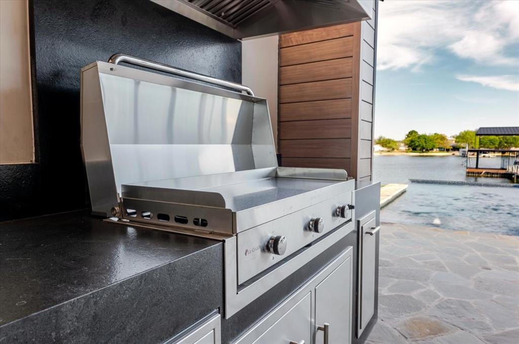 1014 Chaparrel Lane Graford, TX 76449 - Photo 34 of 40 Outdoor Kitchen with Premium Flat Grill - This outdoor kitchen is anchored by a professional-grade 40” Le Griddle flat grill, perfect for everything from sunrise pancakes to sunset smashburgers. A built-in warming drawer keeps dishes at the ready while guests gather, and ample cabinetry provides storage for grill-side essentials. Finished with sleek black counters and framed by the same durable wood-look steel siding featured on the home, this space is as functional as it is stylish—ready for poolside cookouts or lakeside lounging.