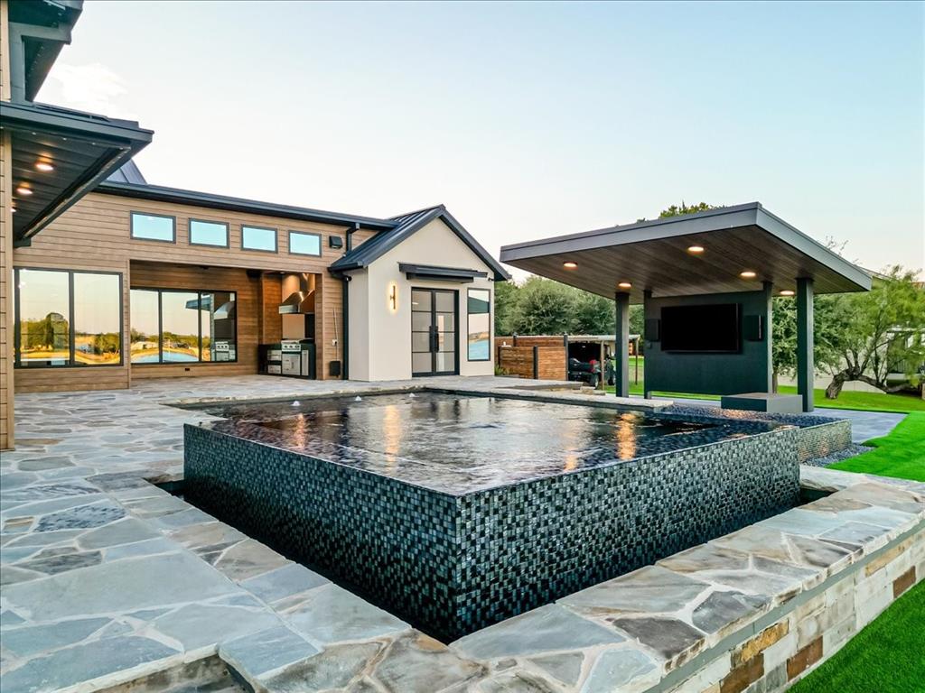 1014 Chaparrel Lane Graford, TX 76449 - Photo 35 of 40 Where Architecture Meets the Horizon - Every angle of this backyard was designed to impress—from the textured tile of the zero-edge pool to the rich façade and floating pavilion. With the lake as its ever-changing backdrop, this outdoor space isn’t just beautiful—it’s intentional. A seamless fusion of structure, water, fire, and sky, it’s a place where form meets function and everyday moments feel like a luxury retreat.