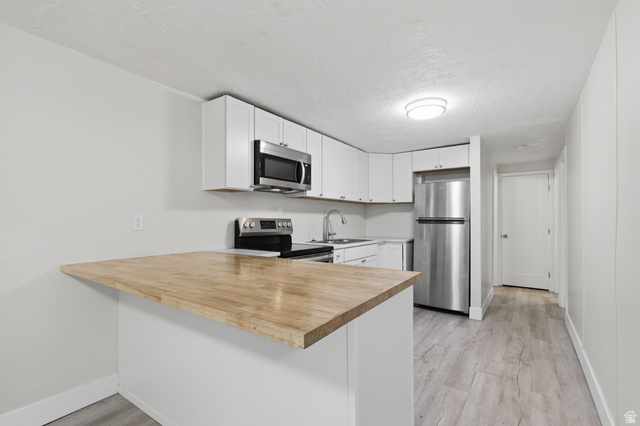 831 Lennox Street, Unit 5 Midvale, UT 84047 - Photo 9 of 19 Kitchen with a peninsula, stainless steel appliances, light wood-type flooring, white cabinets, and wooden counters