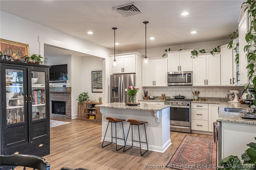 480 Clark Street Southern Pines, NC 28387 - Photo 9 of 28 a kitchen with stainless steel appliances granite countertop a stove top oven a refrigerator a sink and a dining table with wooden floor