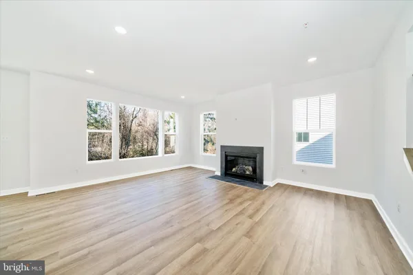 a view of an empty room with wooden floor fireplace and a window