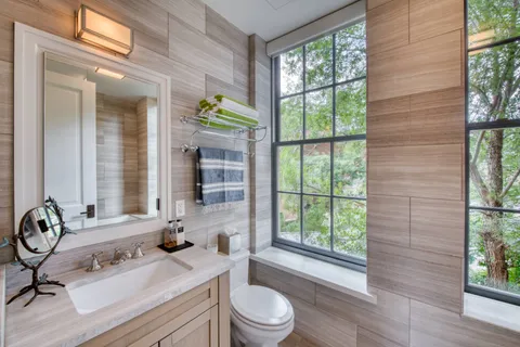 a bathroom with a sink a toilet a mirror and next to a window