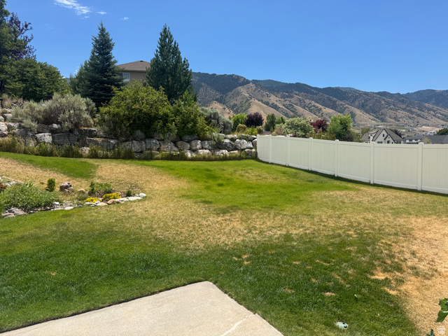 88 Canterbury Lane Logan, UT 84321 - Photo 34 of 37 Expansive backyard featuring a concrete patio, a private white vinyl fence, and a rock retaining wall with mature trees