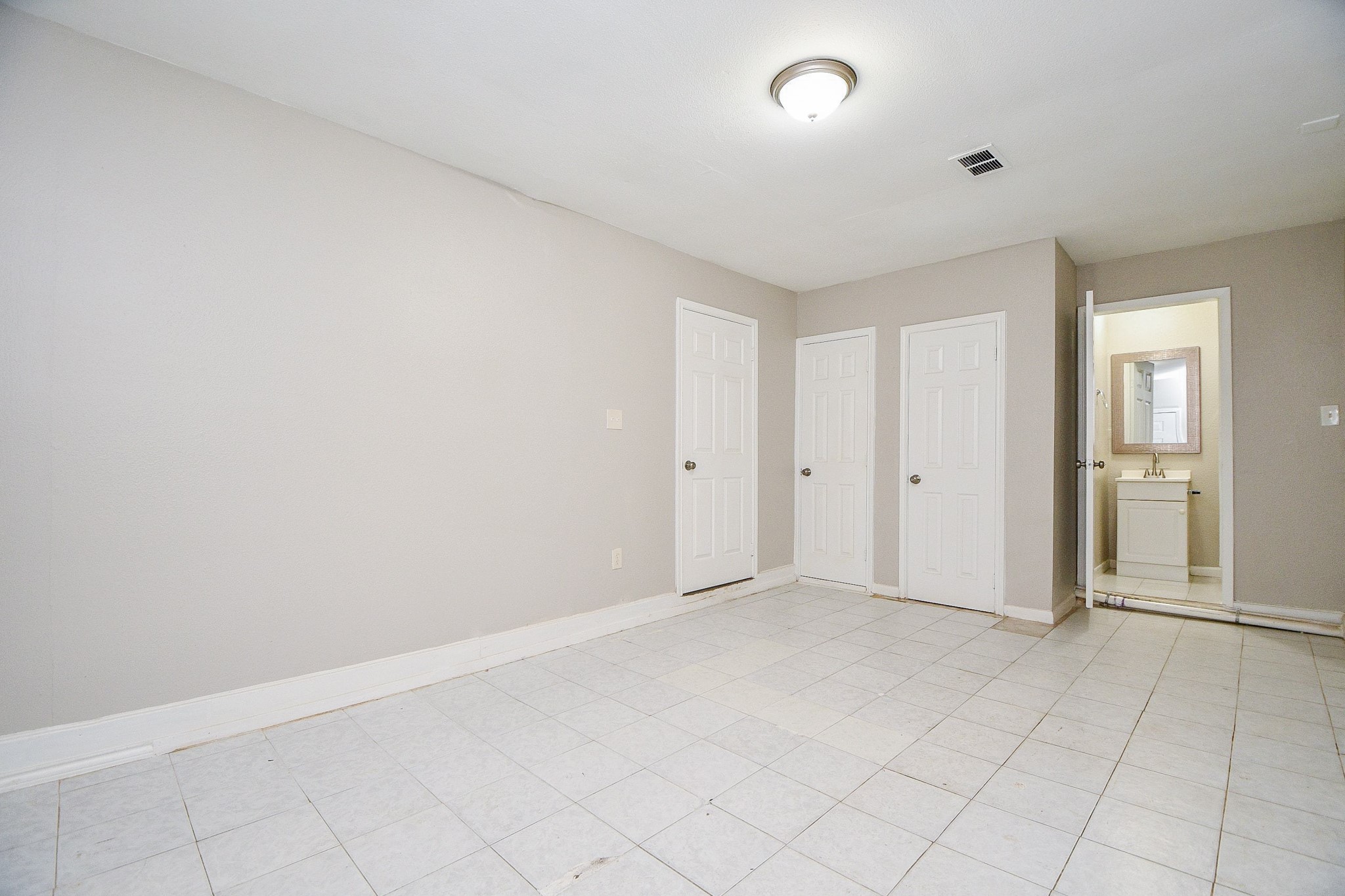 1606 Harris Avenue Pasadena, TX 77506 - Photo 15 of 20 Neutral space with tiled flooring, two closed doors, and an open door to a small bathroom with vanity and ceiling light.