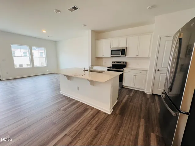 a large kitchen with stainless steel appliances granite countertop a stove a sink dishwasher a refrigerator white cabinets and wooden floor