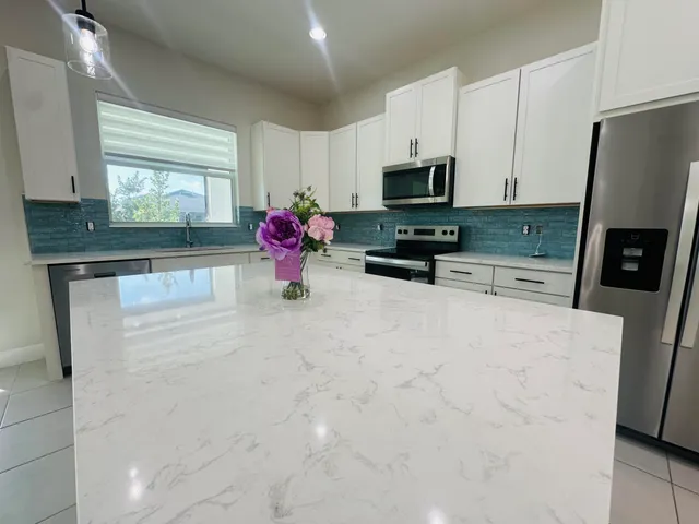 a kitchen with stainless steel appliances a sink a stove a microwave a refrigerator cabinets and a dining table