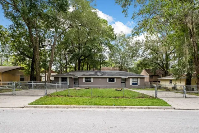 a view of house in front of a big yard with large trees