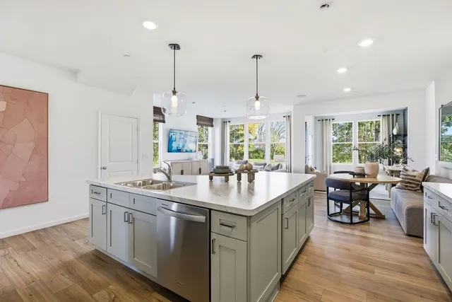 a open kitchen with stainless steel appliances granite countertop a sink a oven a dining table chairs and white cabinets