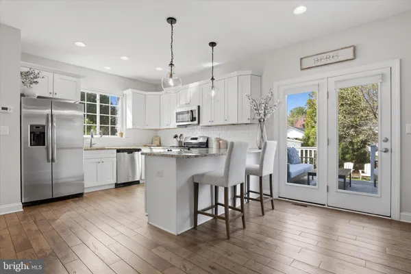 a kitchen with stainless steel appliances granite countertop a refrigerator a sink dishwasher a stove and white countertops with wooden floor