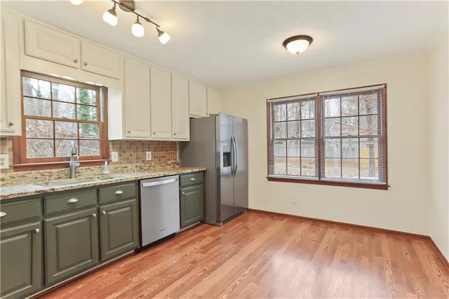 a kitchen with stainless steel appliances granite countertop a refrigerator a sink dishwasher a stove and white countertops with wooden floor