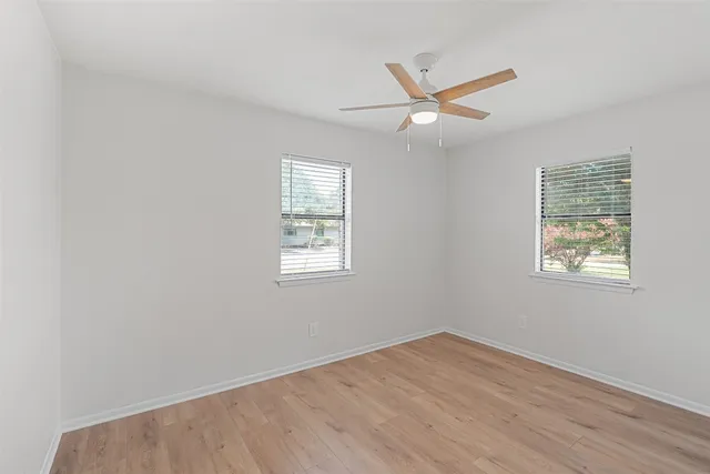 an empty room with wooden floor ceiling fan and windows
