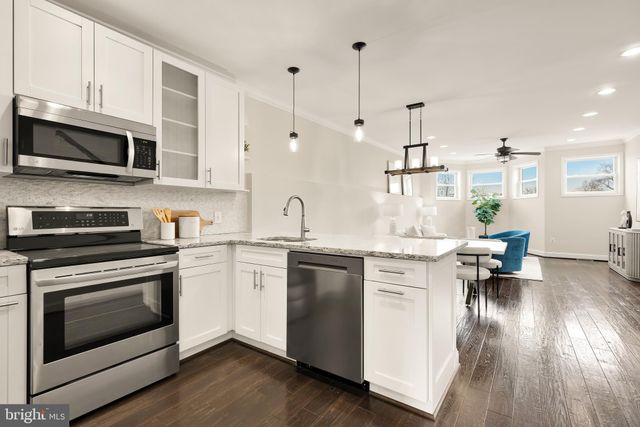 a kitchen with stainless steel appliances white cabinets a sink a stove a microwave and wooden floors