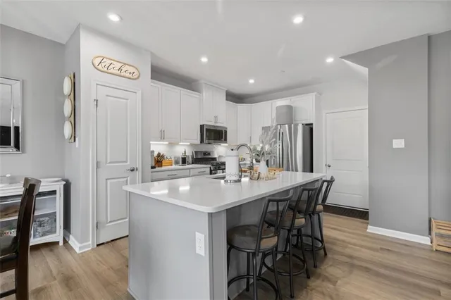 a kitchen with stainless steel appliances granite countertop a stove a sink a microwave a refrigerator and white cabinets with wooden floor