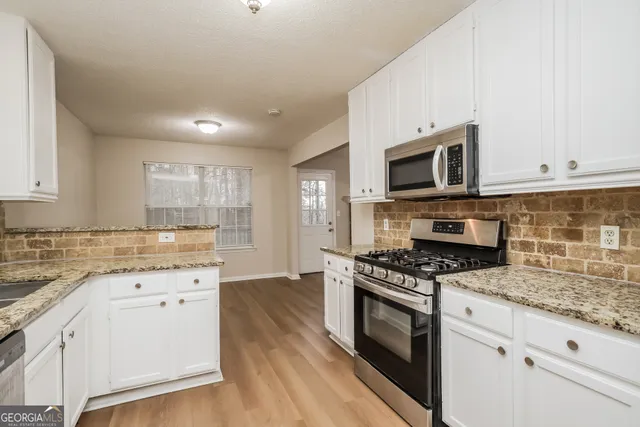 a kitchen with granite countertop a stove top oven a sink dishwasher and white cabinets with wooden floor