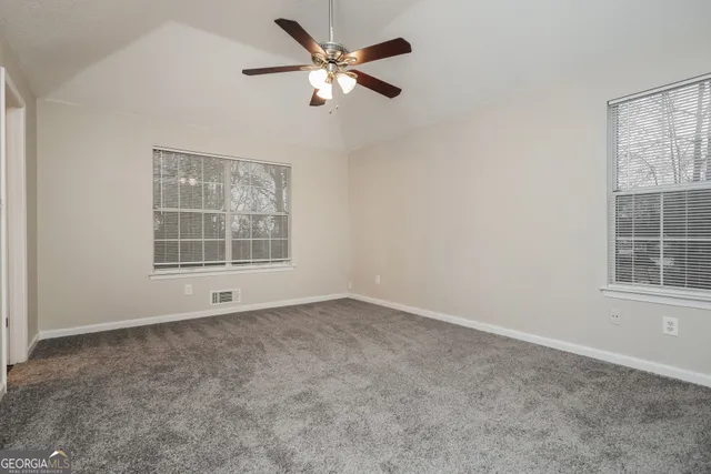 an empty room with chandelier fan and windows