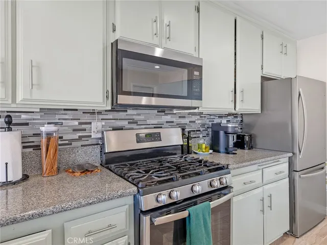 a large white kitchen with stainless steel appliances granite countertop a stove a sink dishwasher a dining table and chairs with wooden floor