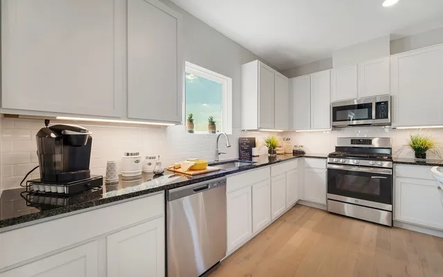 a kitchen with stainless steel appliances granite countertop a sink dishwasher stove and white cabinets with wooden floor