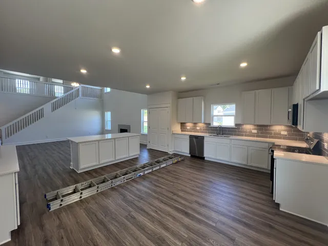 a large white kitchen with kitchen island a sink dishwasher stove and white cabinets with wooden floor