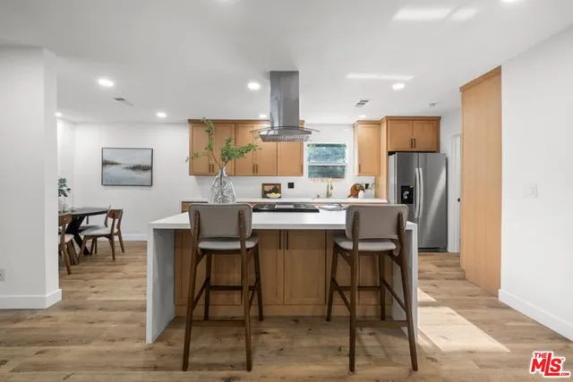 a kitchen with stainless steel appliances kitchen island granite countertop a dining table chairs and a refrigerator