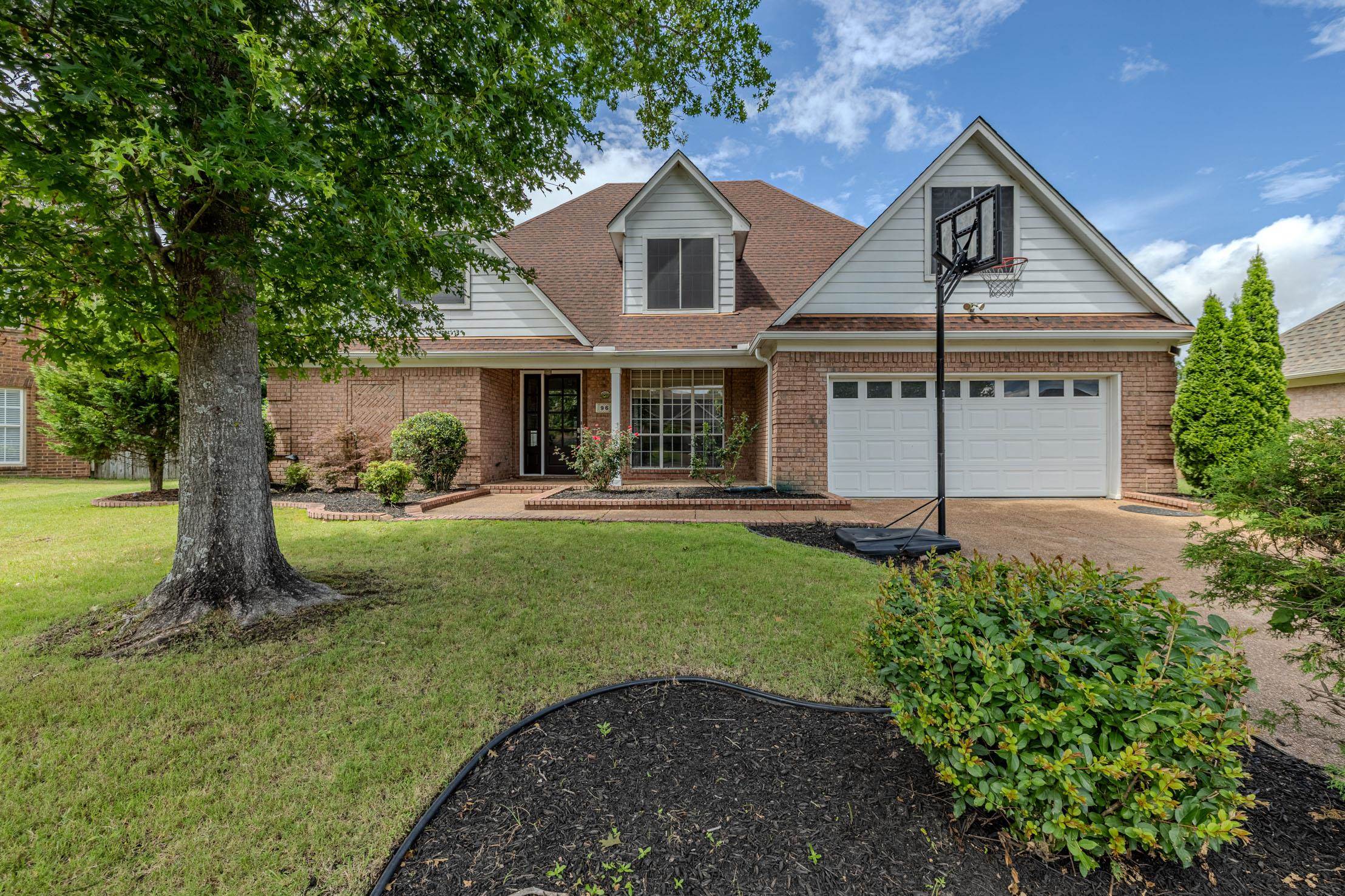 96 Berryfield Cove Collierville, TN 38017 - Photo 38 of 39 Brick and siding exterior featuring a prominent two-car garage with white doors, a dormer window, and mature front yard landscaping
